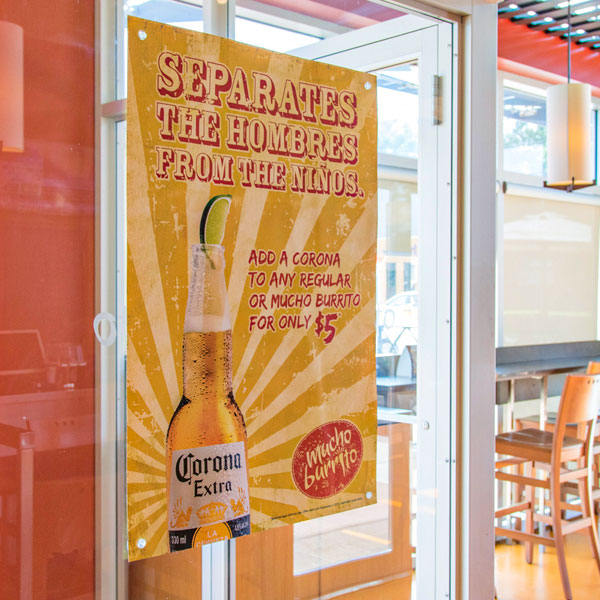 Large format promotional banner featuring a Corona beer bottle with text advertising a special offer at Mucho Burrito, displayed in a vibrant restaurant setting.