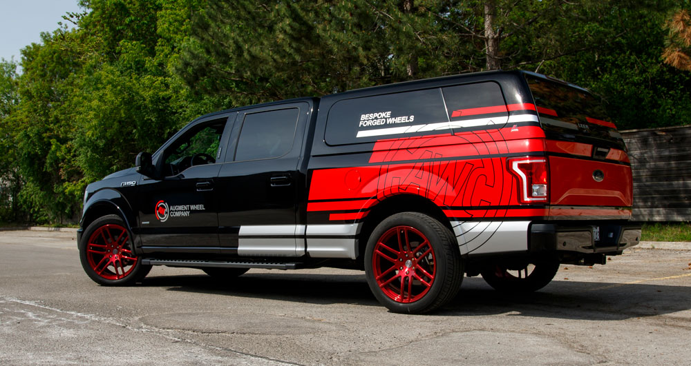 Commercial vehicle with vibrant red and black wrap showcasing Augment Wheel Company branding, parked in an outdoor setting, emphasizing vehicle fleet marketing potential.