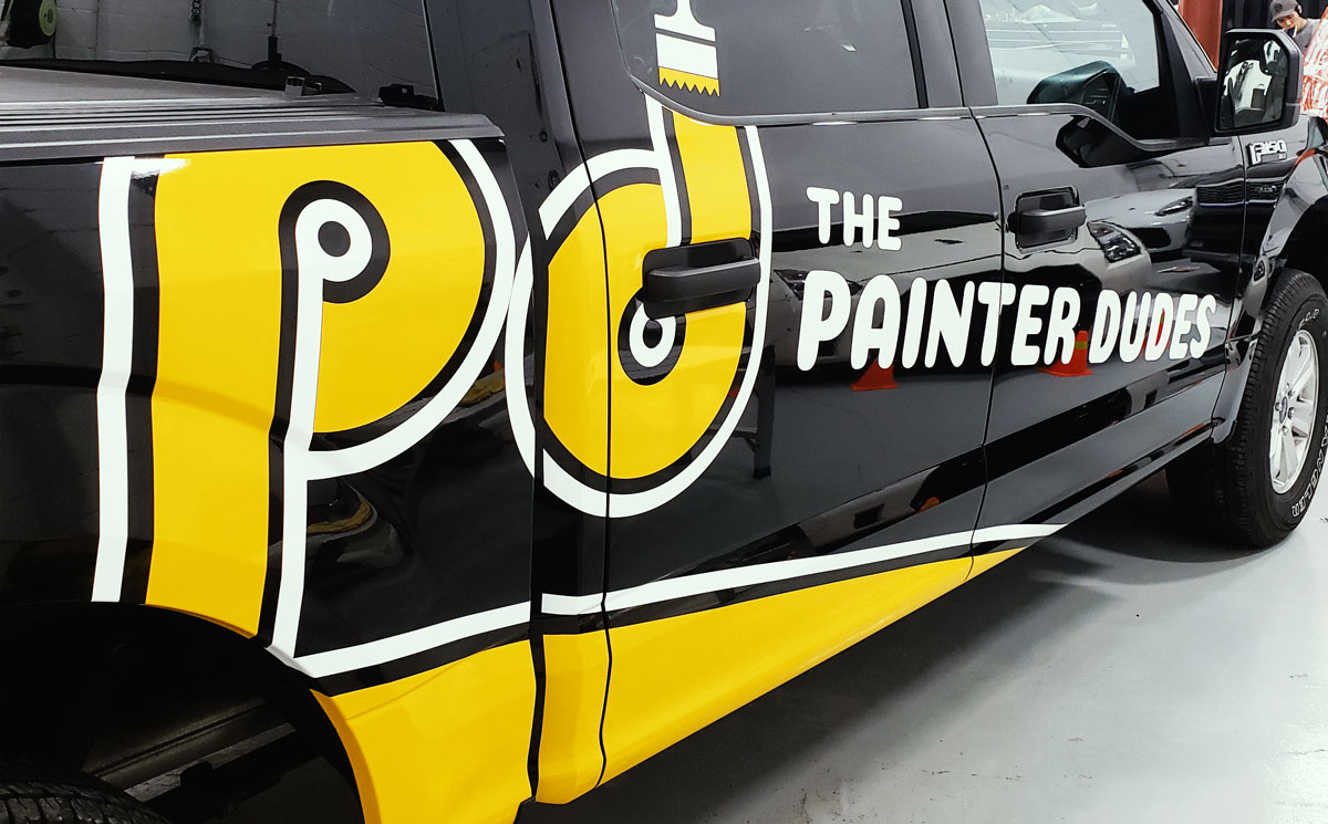 Commercial vehicle wrap featuring "The Painter Dudes" logo in bold yellow and white on a black truck, showcasing effective branding for advertising purposes.