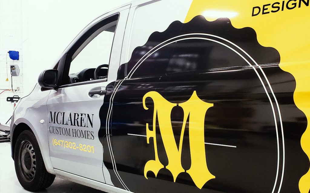 Commercial vehicle wrap featuring "McLaren Custom Homes" branding, black and yellow design, and contact number for advertising purposes.